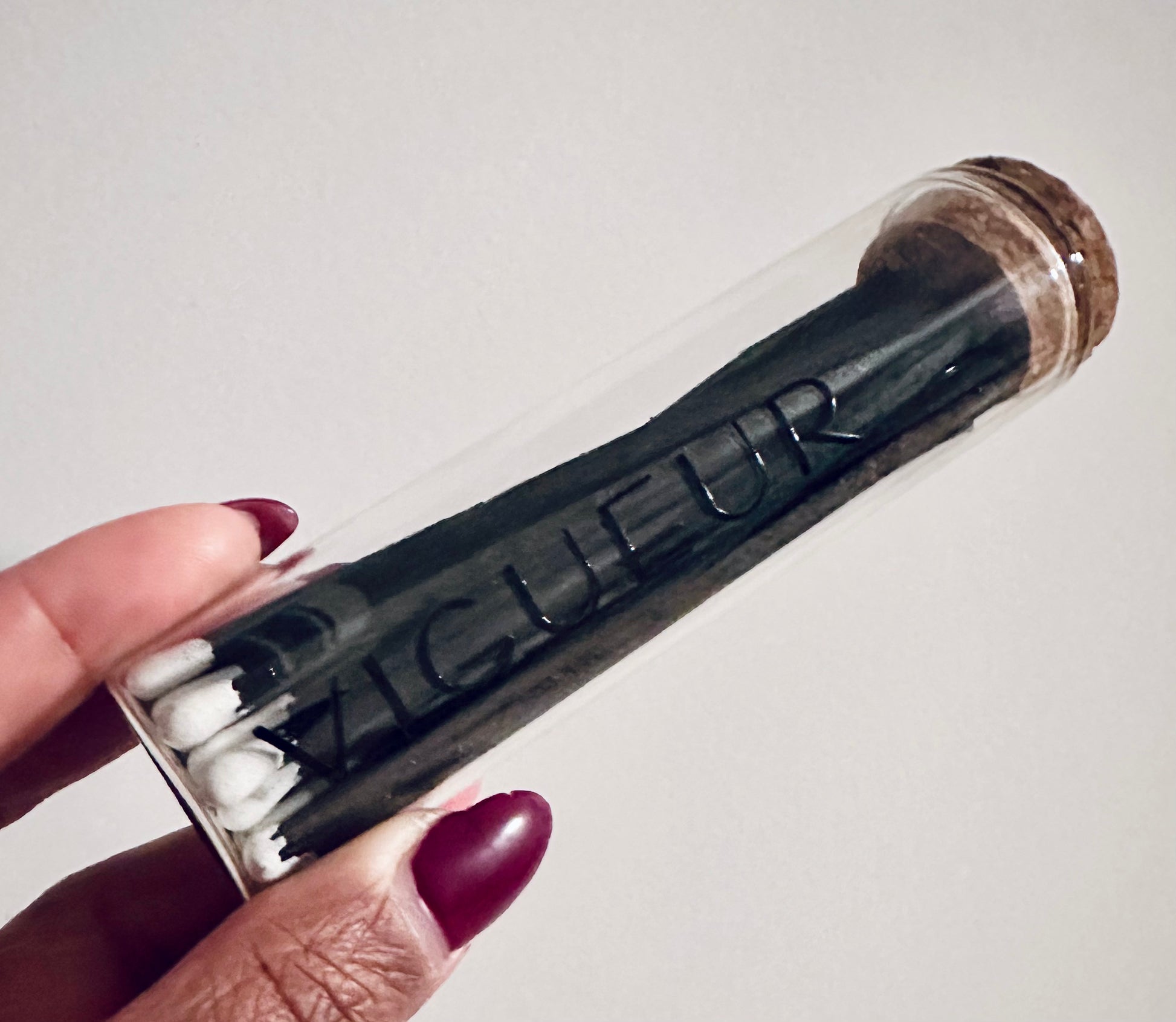 Person holding a glass vial filled with matches labeled 'Vigueur' 