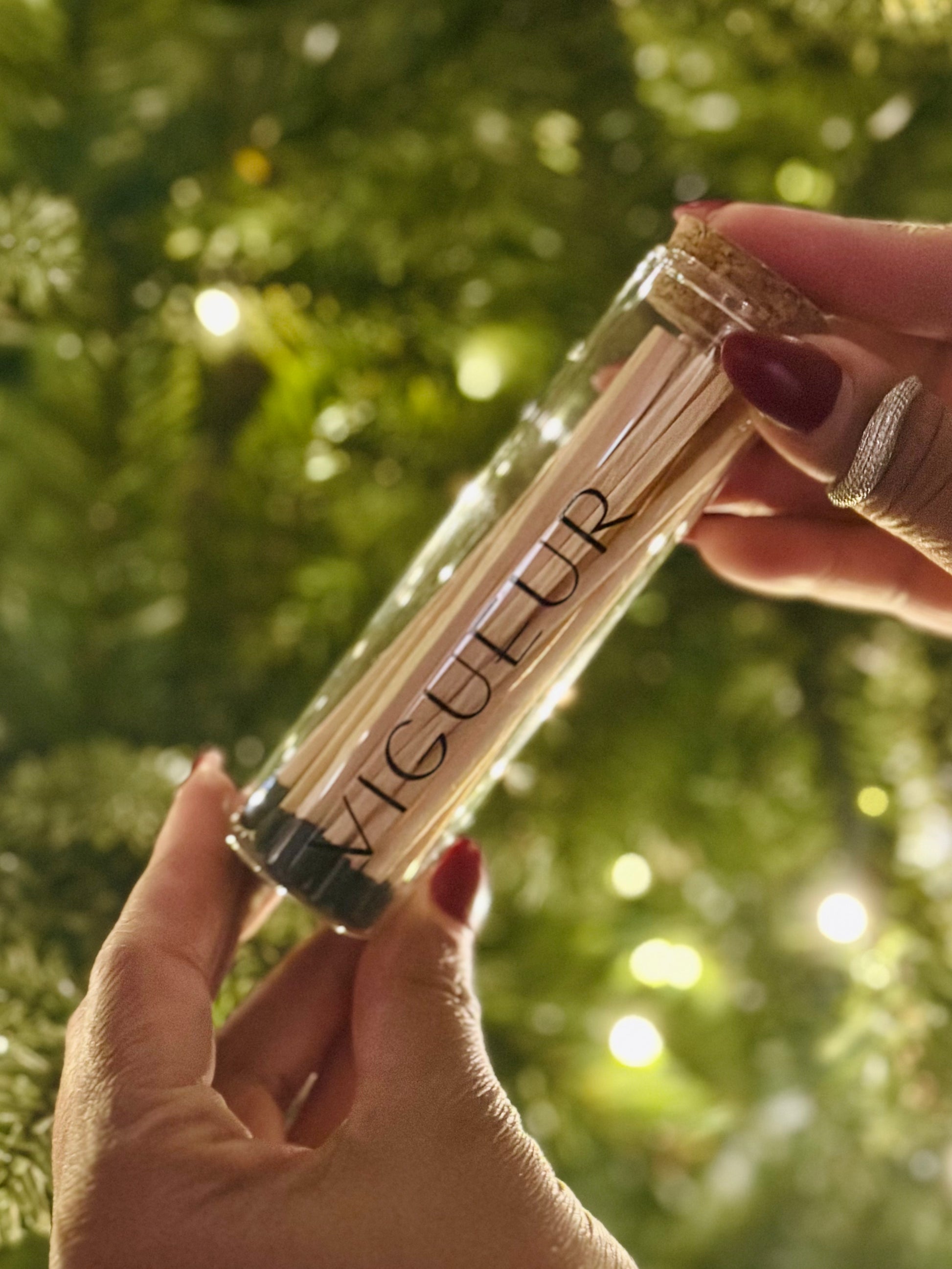 Person holding a glass vial filled with matches labeled 'Vigueur' 